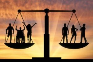 Picture of balance scales with three disabled people (one in a wheelchair, one on crutches and another with an invisible disability) in one pan, three none-disabled people in the other pan. The scales are balanced. They are viewed in silhouette against a golden sunset sky.