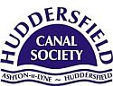 Huddersfield Canal Society logo. All blue on a white background. The word "Huddersfield" wrapped above a blue semi-circle, the bottomof which is wavy, suggesting water. White words "Canal Society" are inside. Underneath, in a wavy ribbon, are the words "Ashton-u-Lyne - Huddersfield".