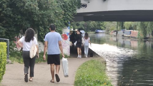 Busy towpath scene, with people walking in both directions along the canal and passing under a bridge