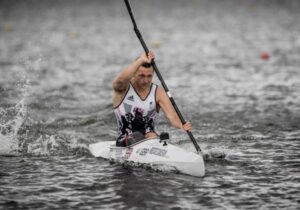 Rob Oliver - Paralympic Kayaker. Picture showing Rob in a white vest powering his white kayak through the water.