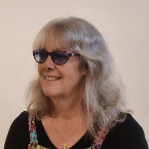 Tracey Clarke, Founder AWA. A middle-aged lady wearing dark glasses (as she is registered Severely Vision Impaired) with shoulder length light grey hair and a black top.