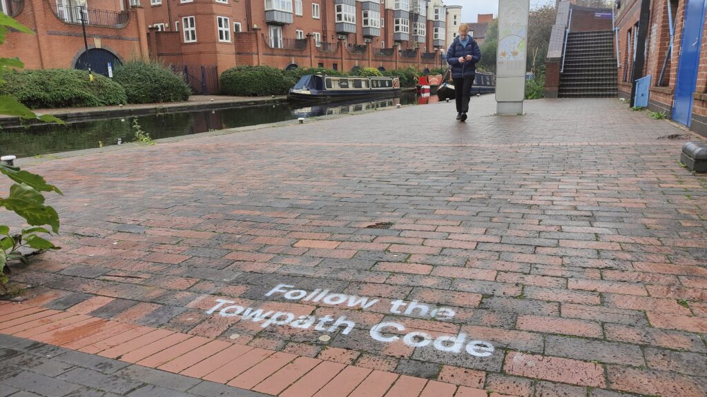 White stencilled sign "Follow the Towpath Code" on a brick towpath.