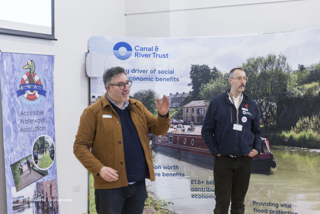 Dick Vincent, wearing a brown jacket, and Matthew Symonds, wearing a blue CRT fleece, standing in front of their banner for their presentation.