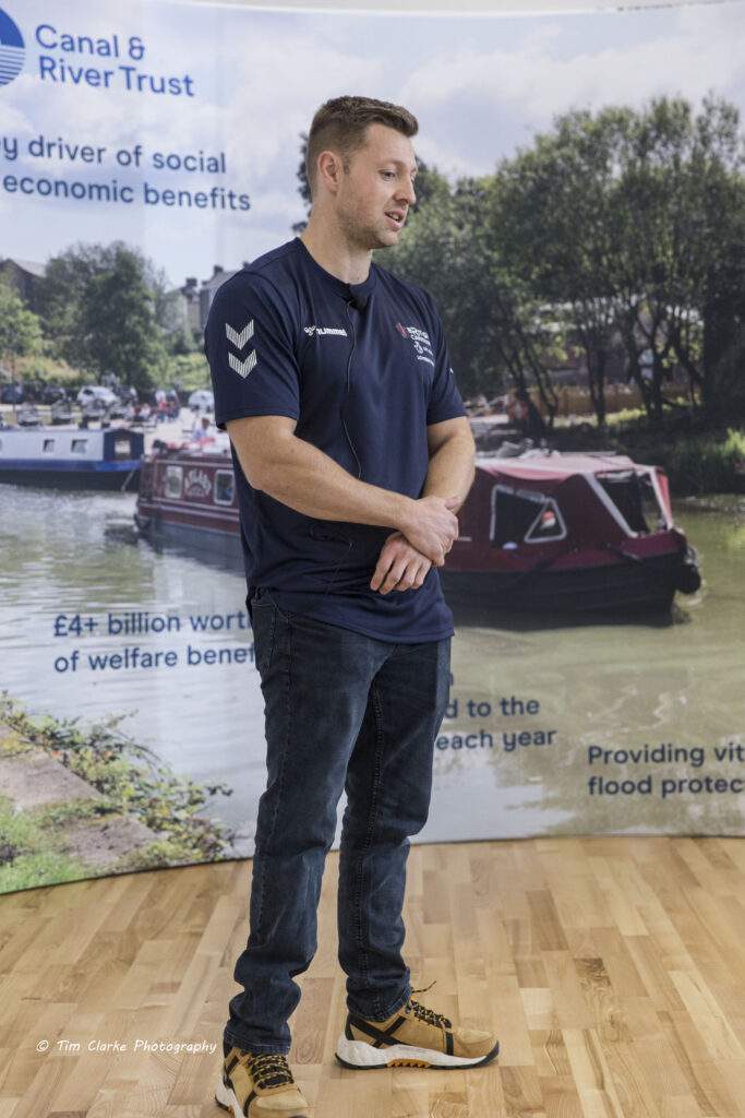 Rob Oliver, wearing blue t-shirt and trousers, standing in front of the CRT banner.